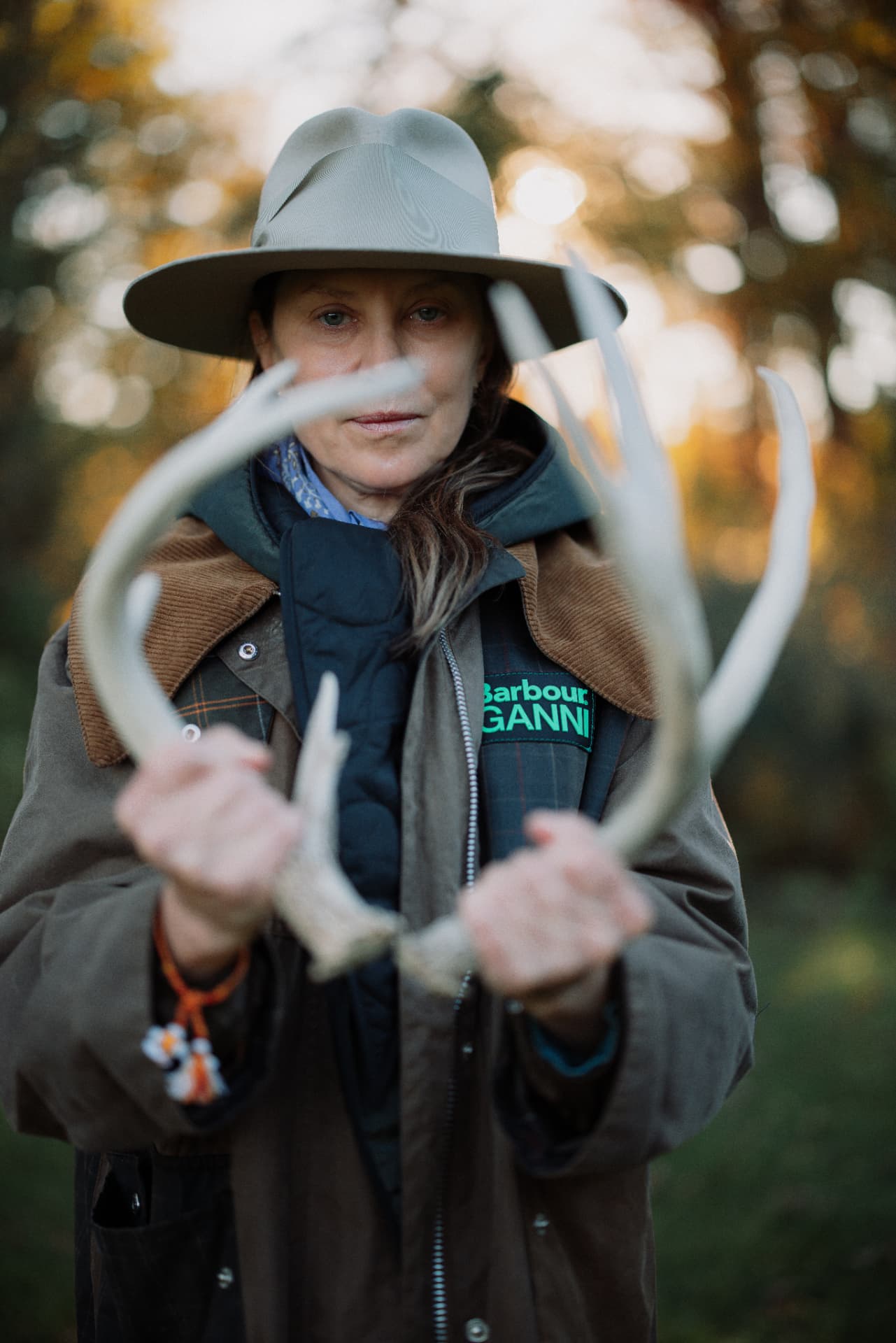 A woman in a pale hat holding antlers among autumn trees