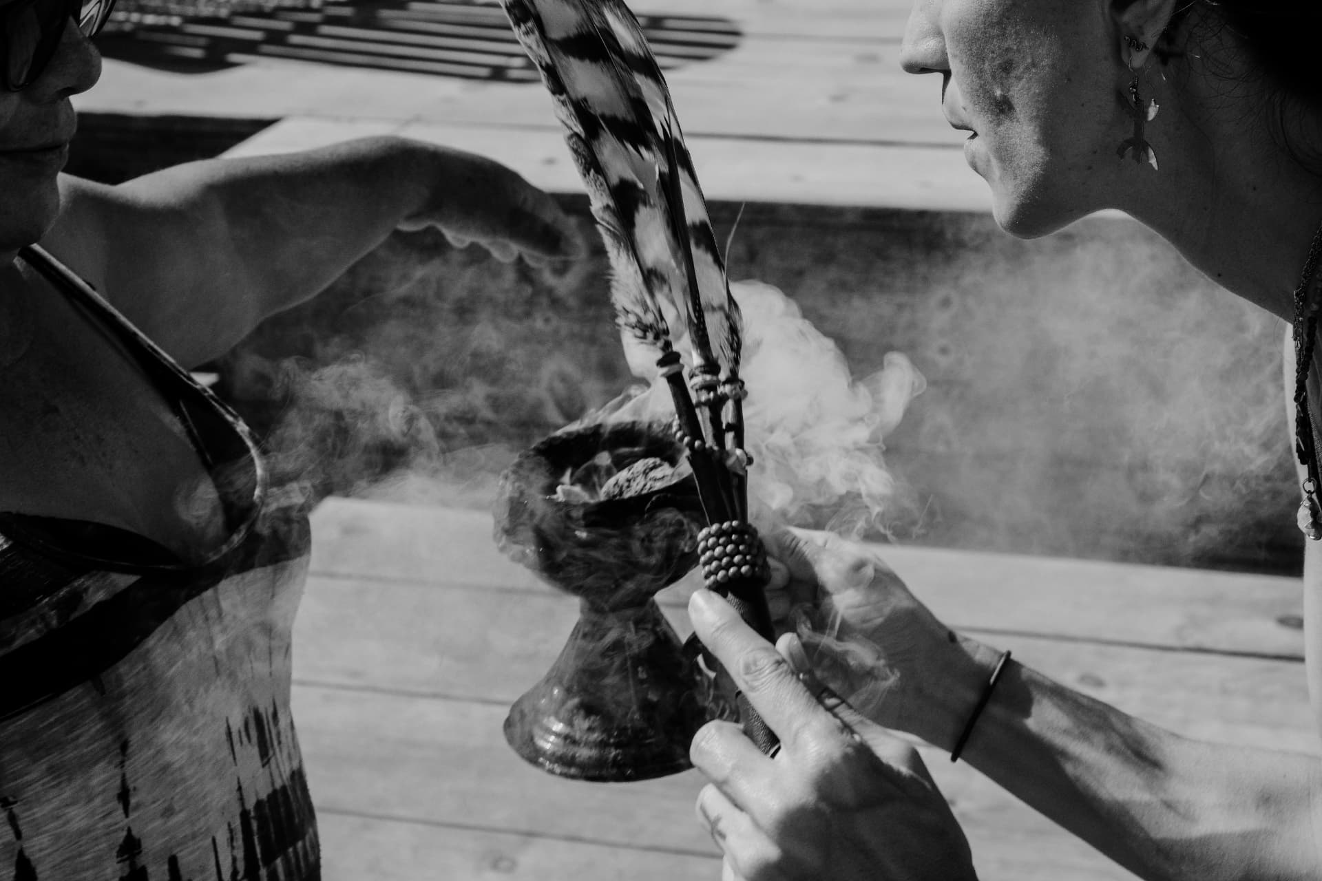 Hands holding a smoking ritual bowl beside a feather fan, in black and white
