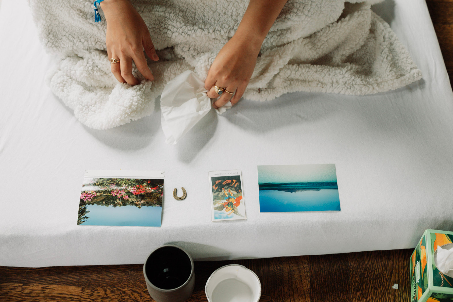 Hands beside photographs, a small horseshoe and a card arranged on a white mattress