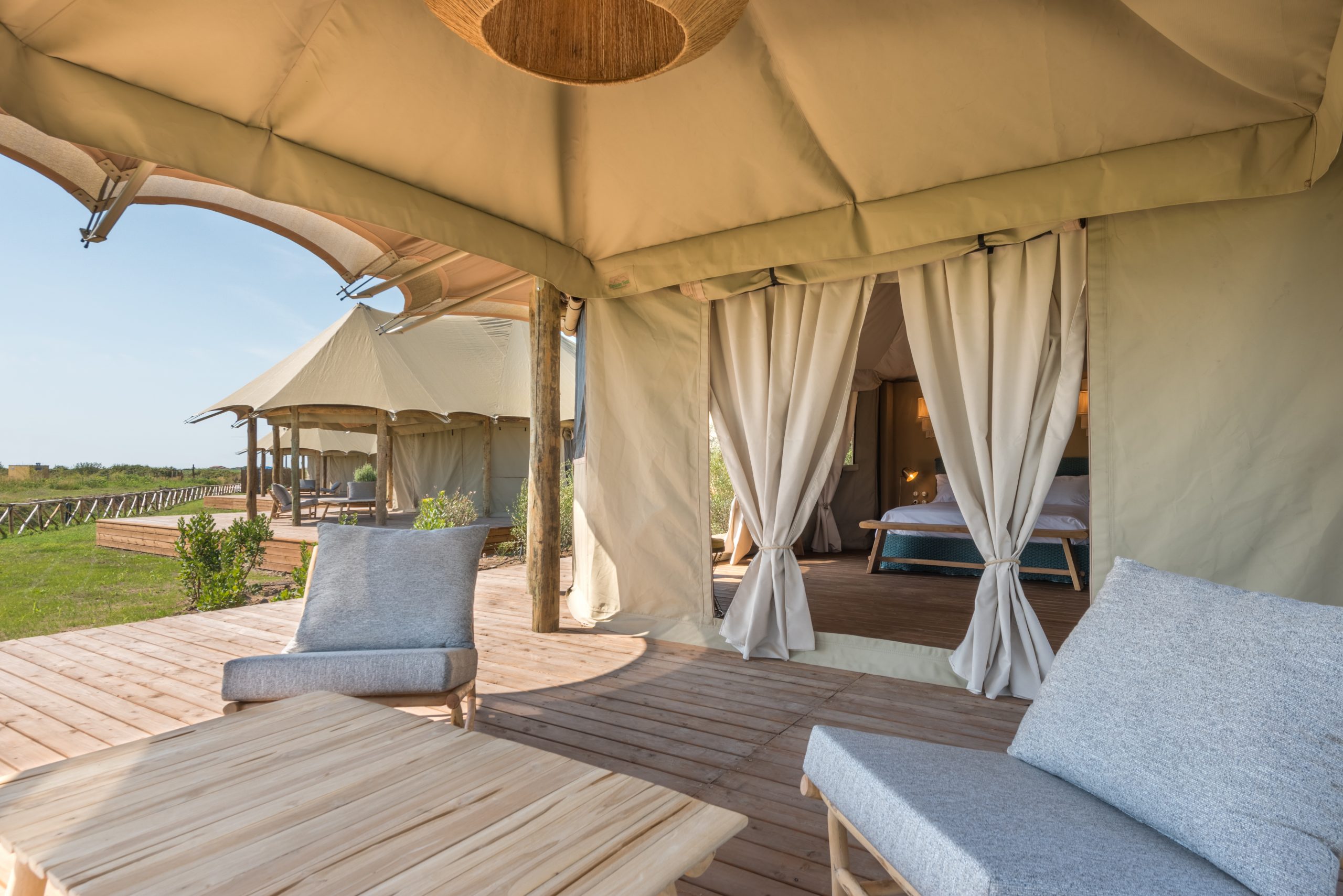 A shaded tent veranda with armchairs and a low wooden table facing the garden