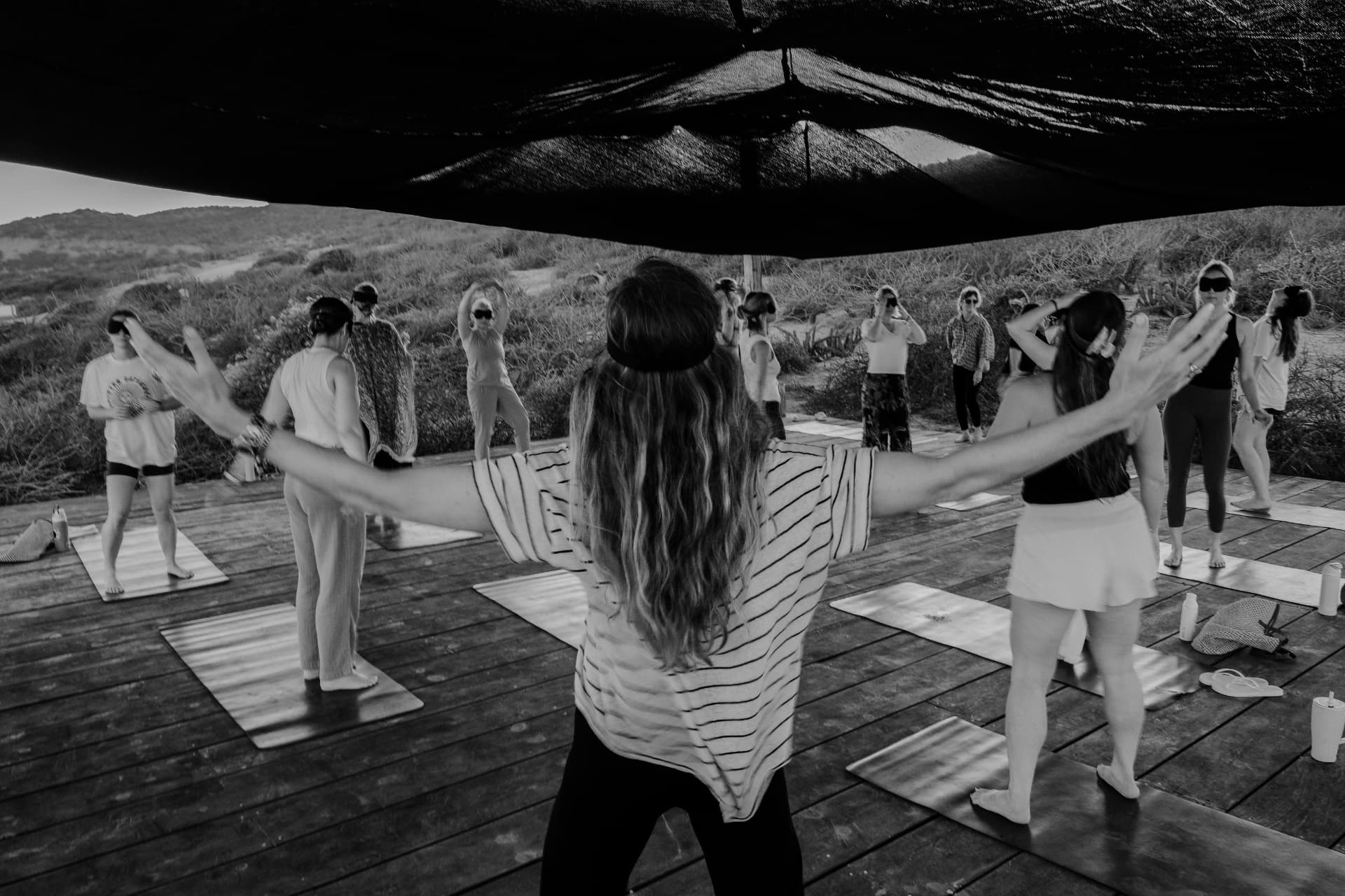 Women moving with outstretched arms on a deck overlooking the sea, in black and white