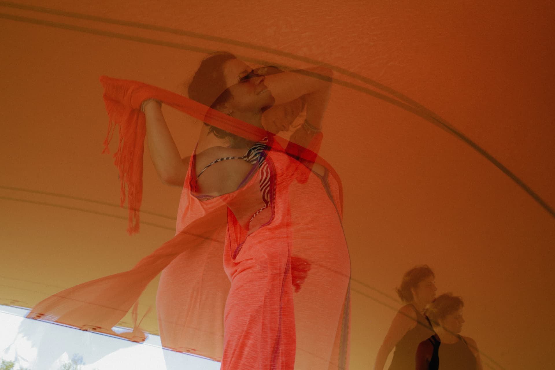 A woman moving with a sheer scarf beneath a saffron canopy