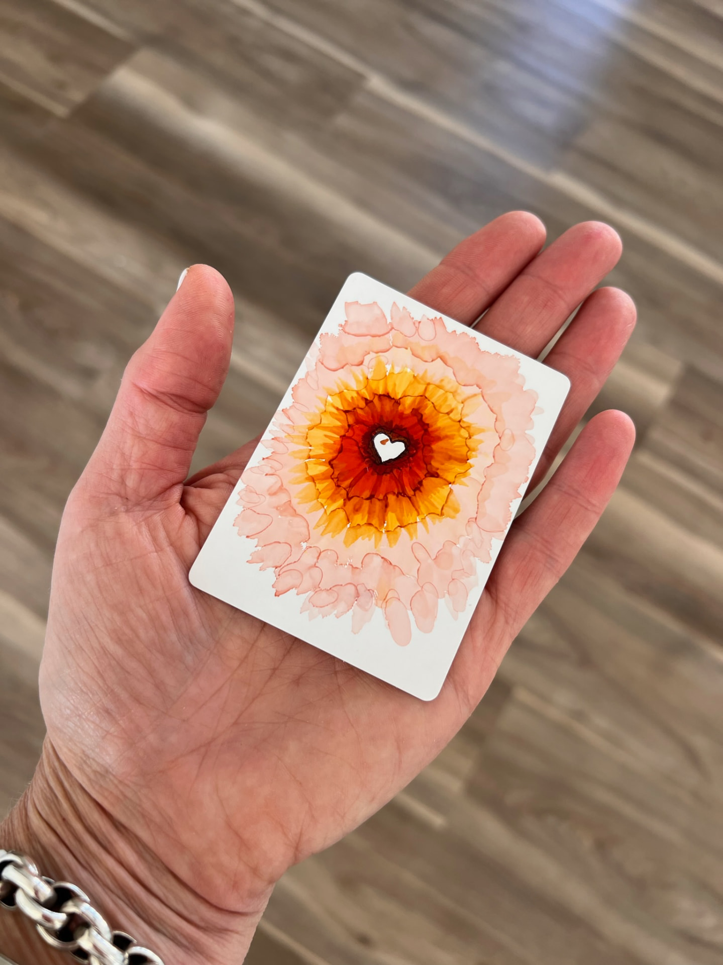 A hand holding a painted flower card with a heart at its center