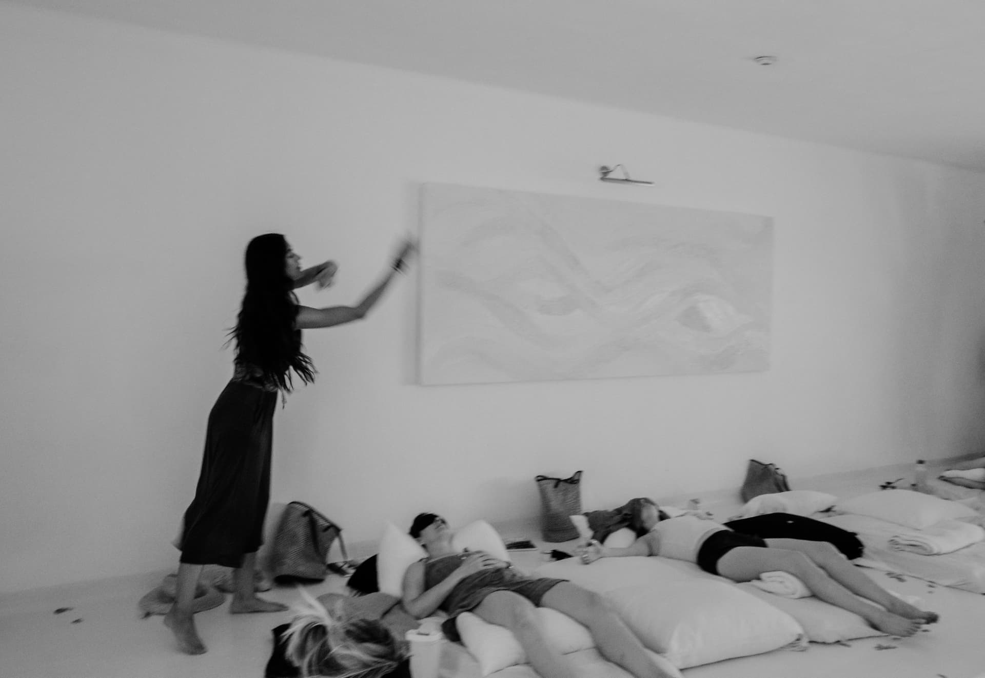 A woman standing with an arm raised beside women resting on cushions, in black and white